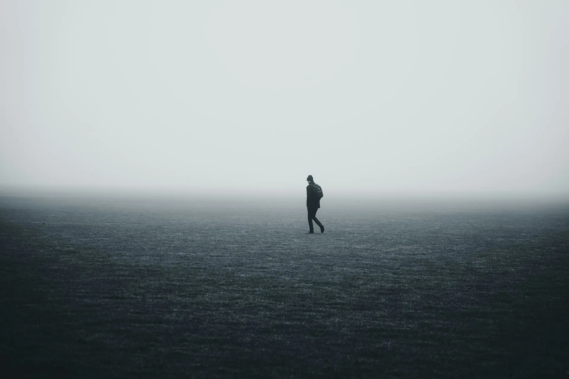 Silhouette of a man walking alone on a foggy open field.